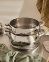Two-tiered Mami stainless steel steaming pots by Alessi, stacked on a metal surface, with green and plaid kitchen towels.