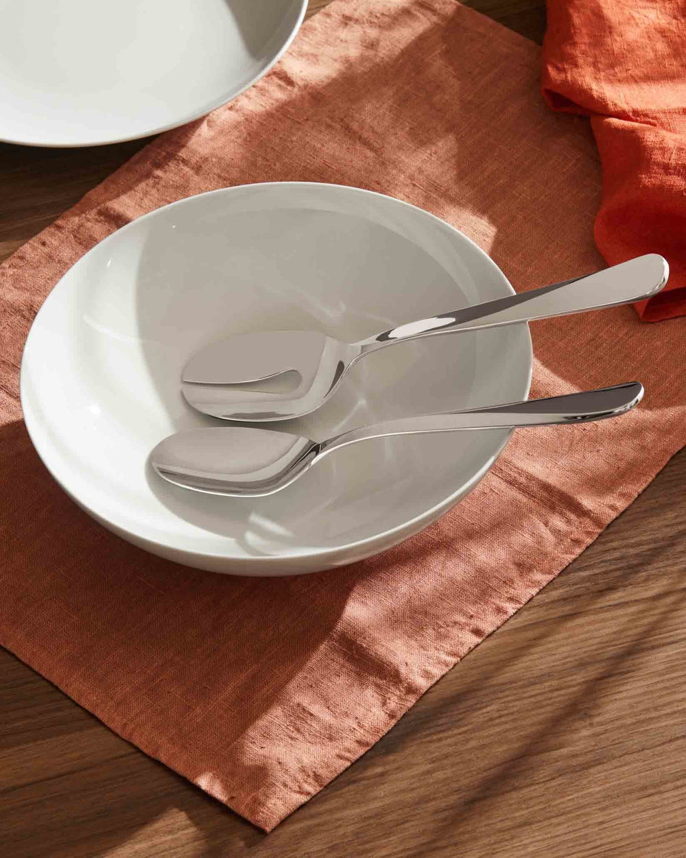 Mami stainless steel serving set by Alessi, polished and resting in a white bowl on an orange linen napkin.