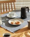 Black Moka pot by Alessi, with a sleek, modern design, on a gray placemat amidst a breakfast setting.