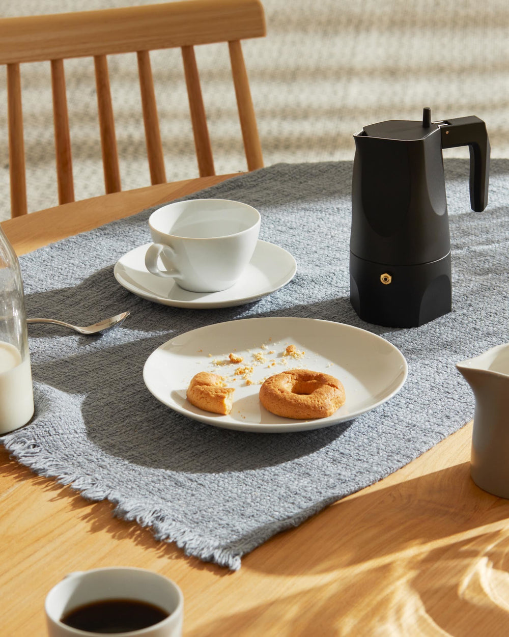 Black Moka pot by Alessi, with a sleek, modern design, on a gray placemat amidst a breakfast setting.