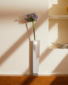 A polished silver Crevasse vase by Alessi, featuring an angular geometric design, holding a single purple flower.