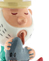 Gnome-like figurine by Alessi, with yellow hat, pink face, white dashed beard, closed eyes, licking a gray heart with '00'.