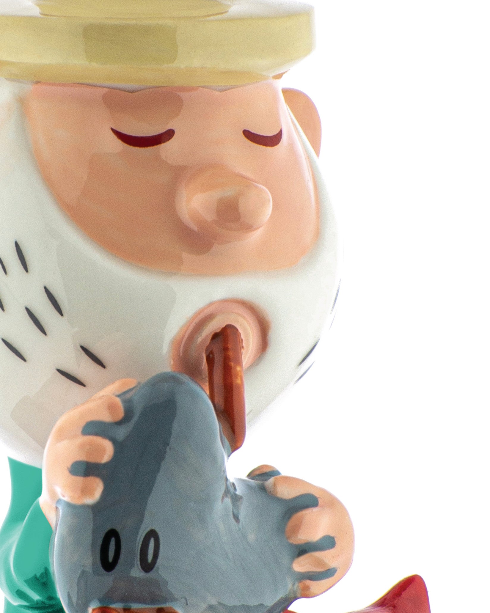Gnome-like figurine by Alessi, with yellow hat, pink face, white dashed beard, closed eyes, licking a gray heart with '00'.