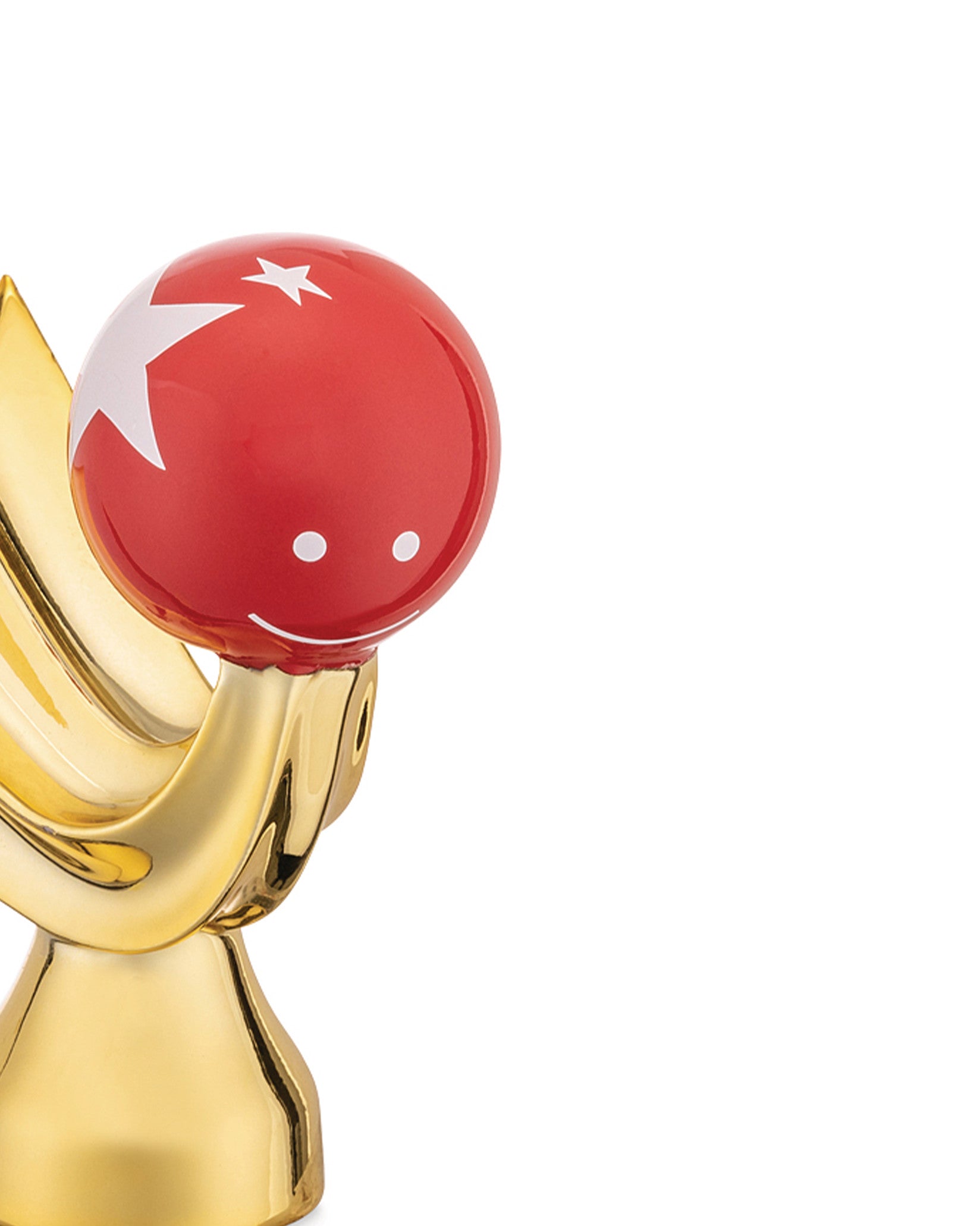 Red Stella Cometa decorative object by Alessi, featuring a white star, smiling face, and glossy gold base.