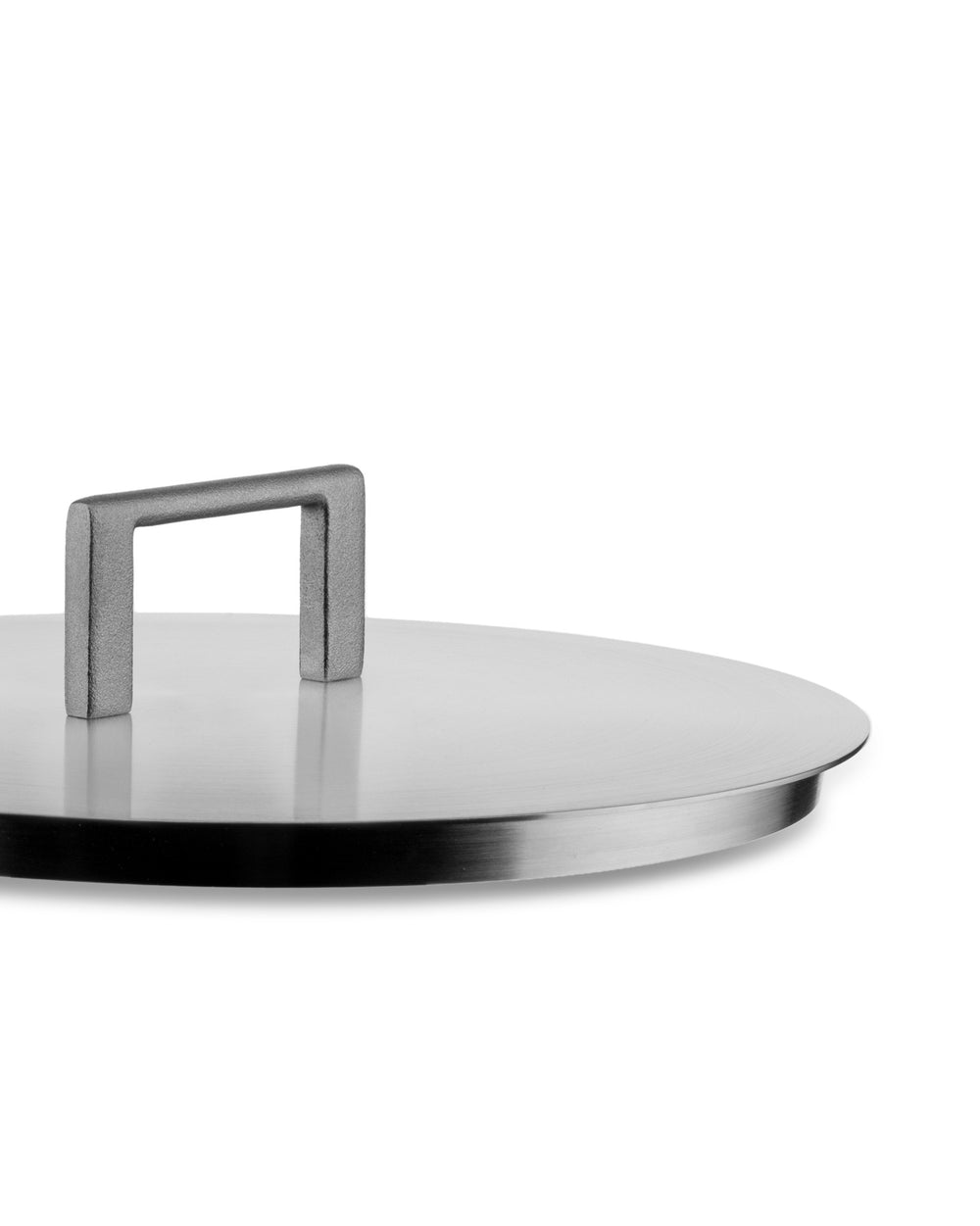 Silver brushed metal round lid by Alessi with a rectangular metal handle, angled view.