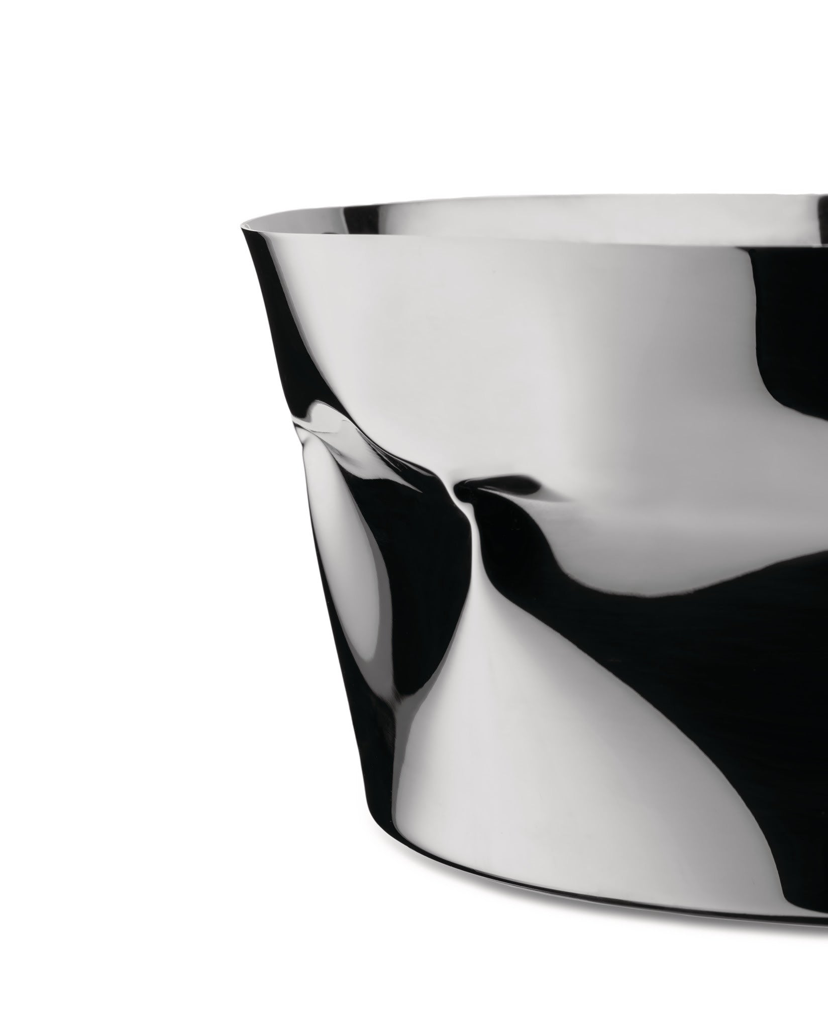A silver sculptural bowl by Alessi, with a highly reflective, crumpled metal surface showing abstract black and white forms.