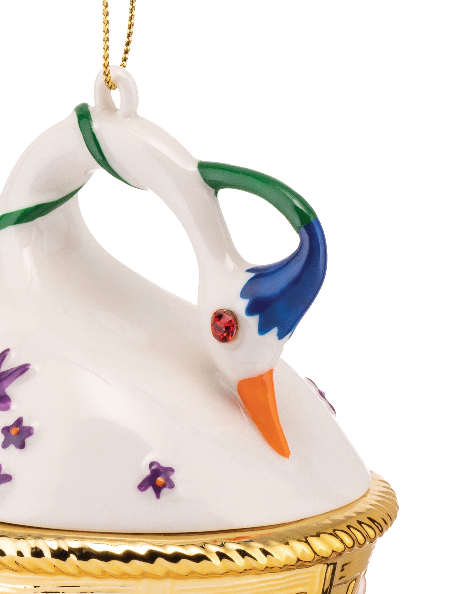 White ceramic swan hanging ornament by Alessi with a red jewel eye, orange beak, blue and green accents, purple flowers, and a golden textured base.