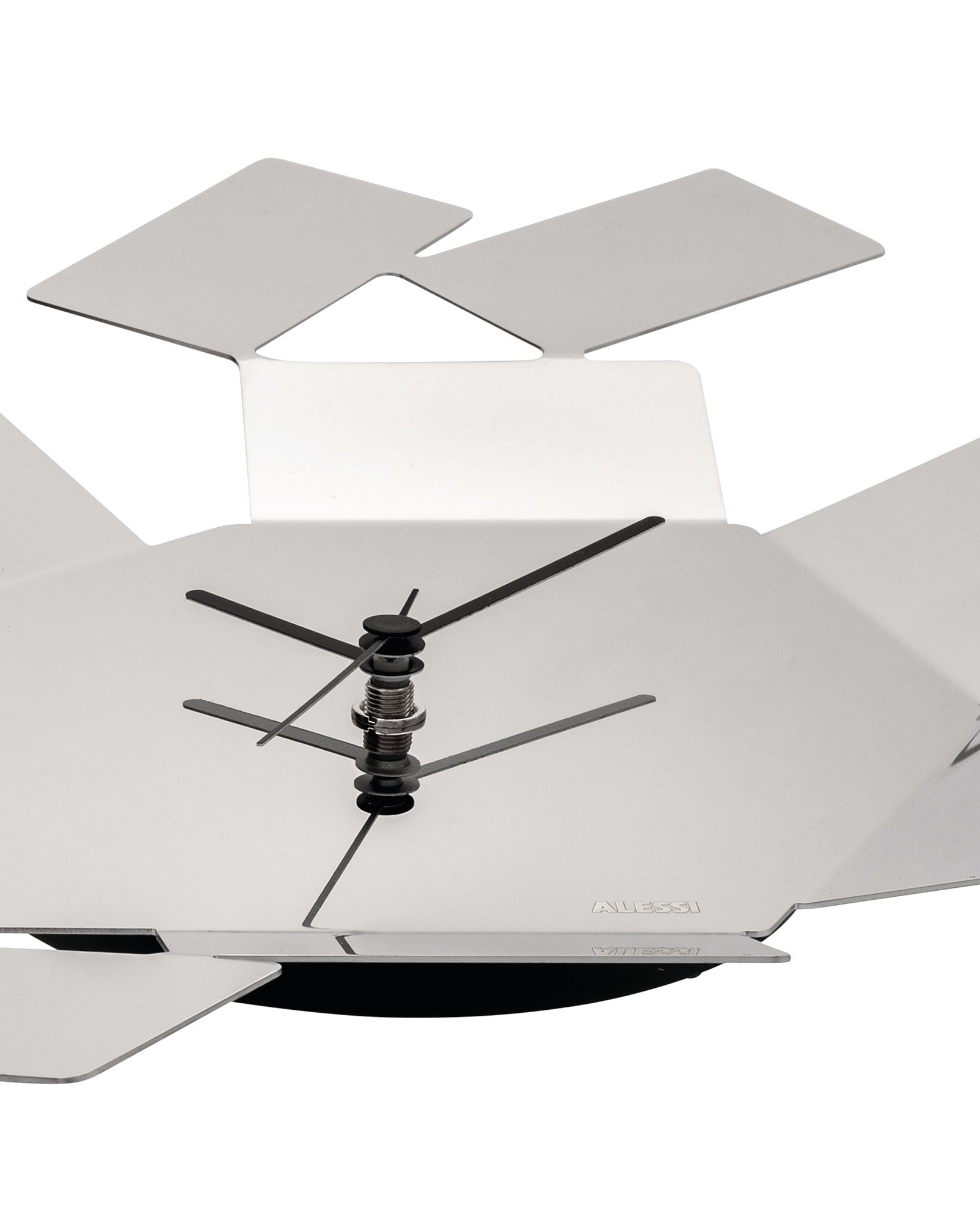 Cropped close-up of a silver-toned metal wall clock by Alessi, featuring an abstract design of radiating geometric panels.