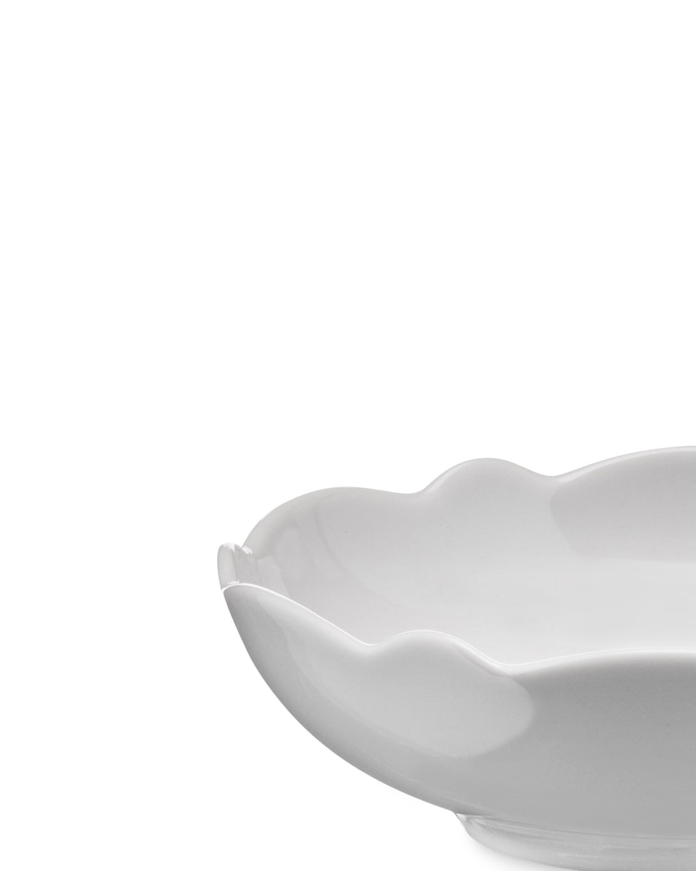 White porcelain serving dish by Alessi with a wavy scalloped rim, viewed from a low side angle.