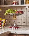 Silver-toned seal figure fruit bowl by Alessi, with a gold sphere and red and white patterned base.