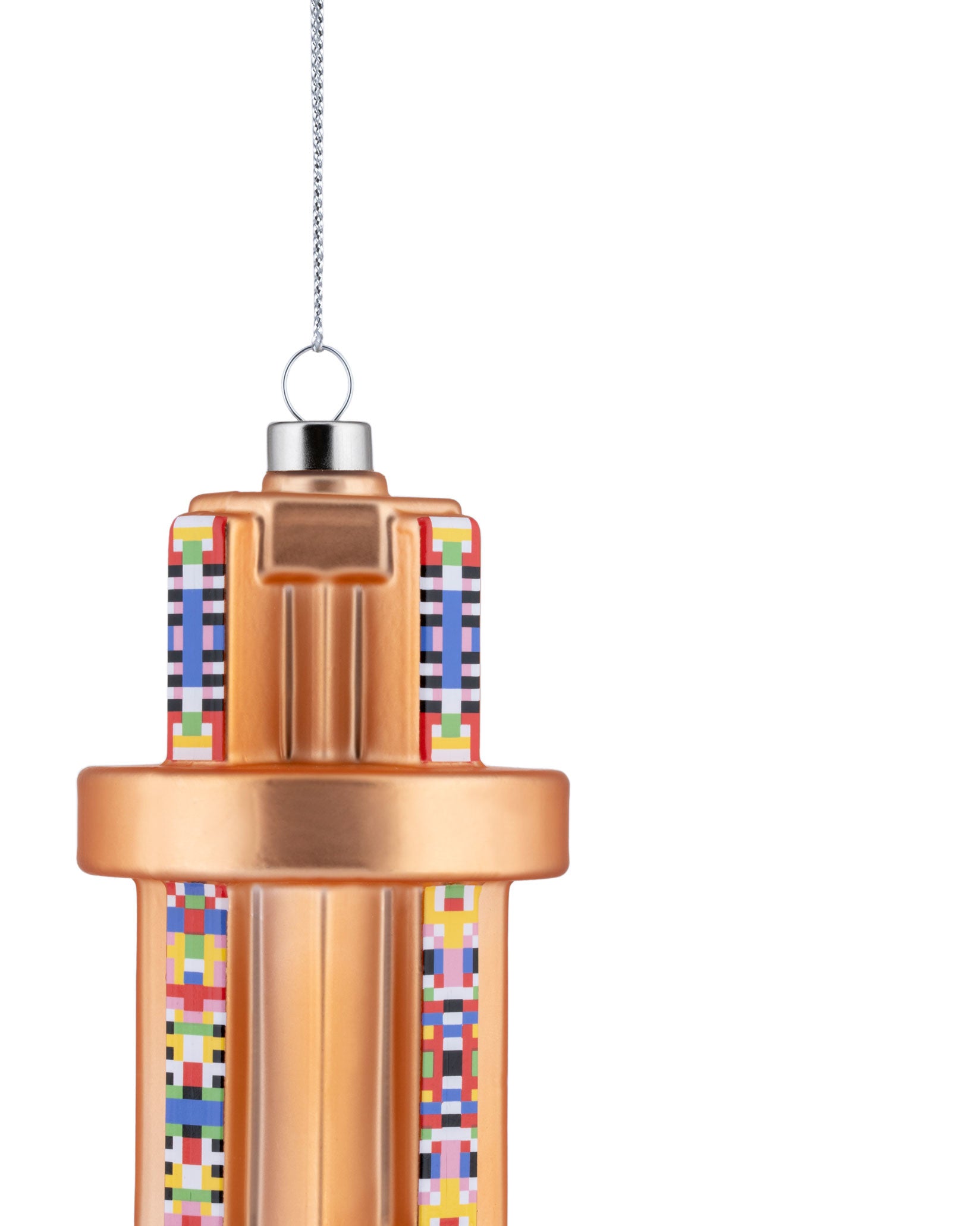 Copper-colored prism Christmas tree ornament by Alessi, with colorful pixelated patterns on vertical panels, hanging.