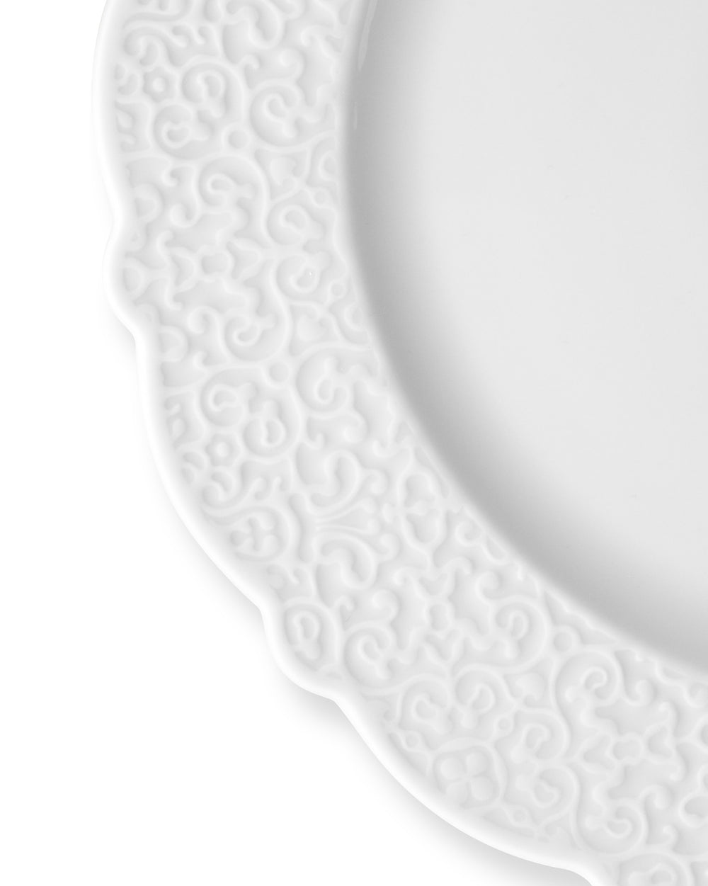 White dinner plate by Alessi with an ornate embossed scrolling pattern on its scalloped rim.