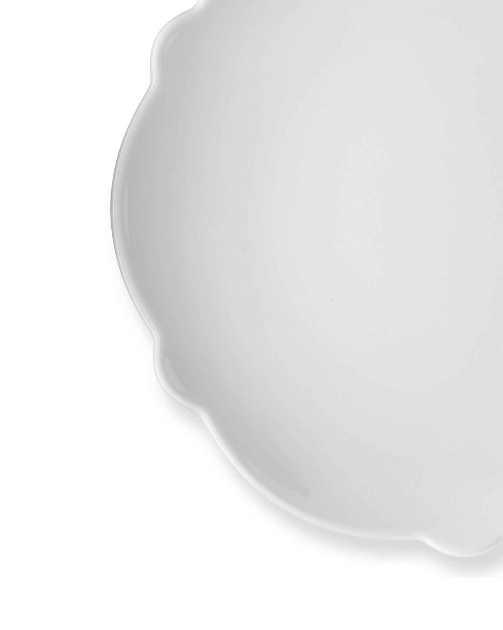 White scalloped plate by Alessi with a glossy finish, shown in a cropped overhead view.