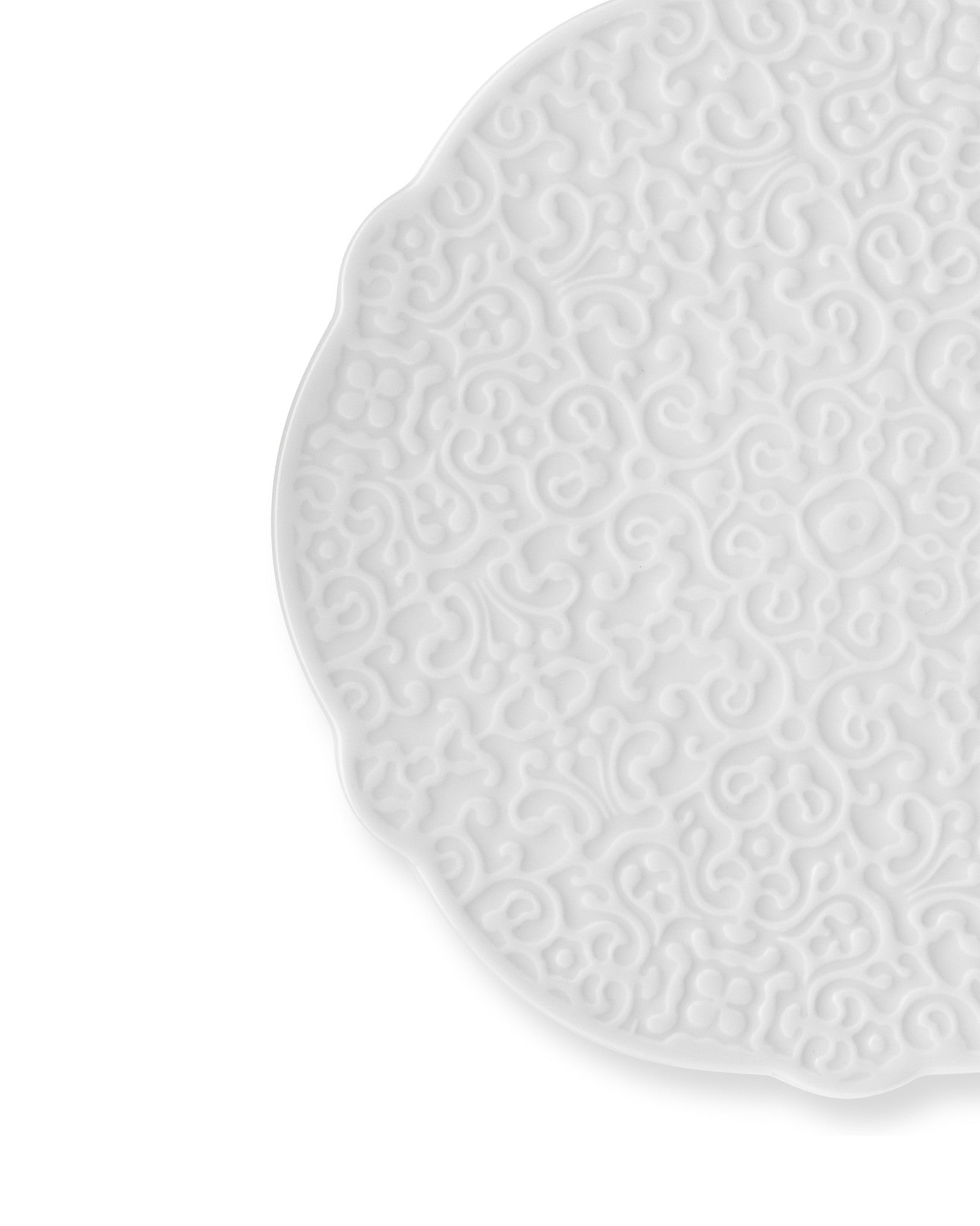 White embossed plate by Alessi with a scalloped edge and intricate scroll pattern, cropped.