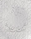 White embossed pattern by Alessi featuring swirling, floral-like designs and a central medallion with a stylized face wearing star earrings.