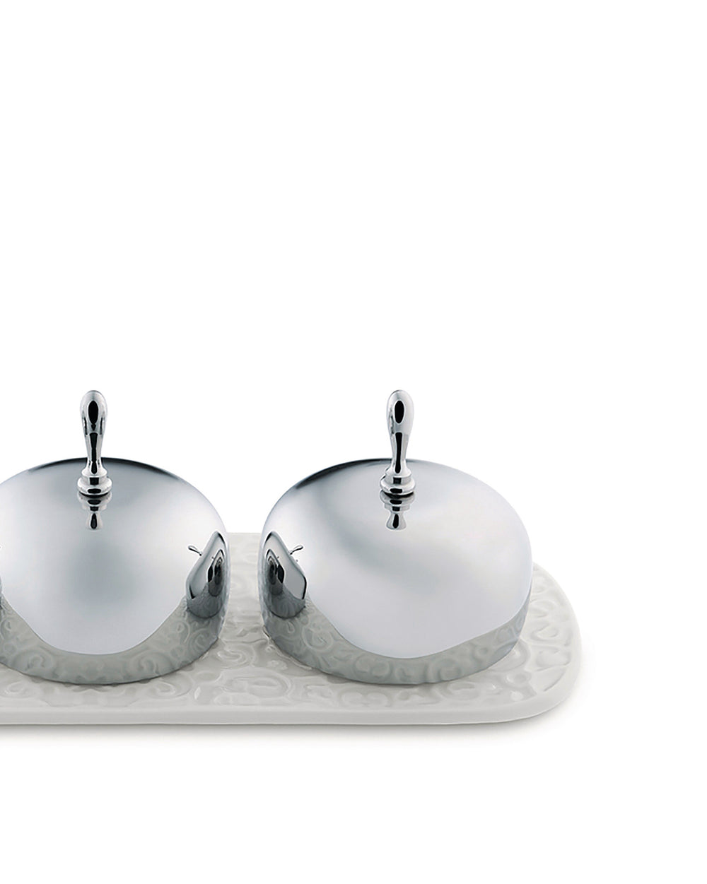 Two chrome butter dishes by Alessi with white embossed ceramic bases on a matching tray.