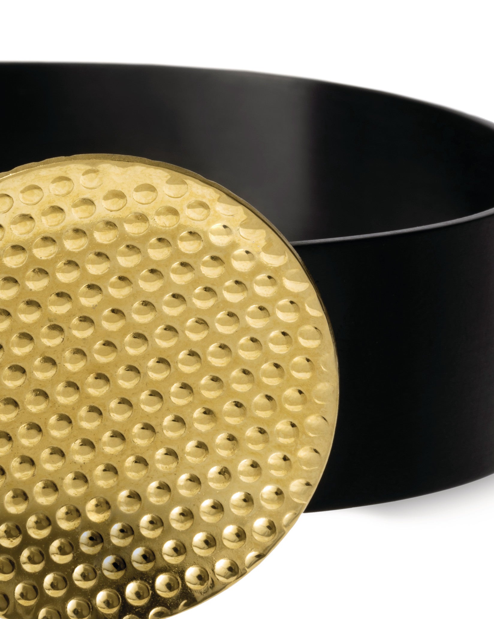 Gold dimpled disc by Alessi, partially covering a curved matte black container.