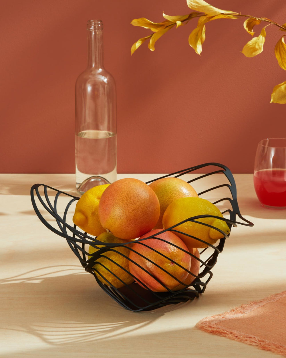Black metal sculptural fruit bowl by Alessi, featuring an abstract wire design filled with lemons and grapefruits.