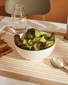 Polished silver serving spoon by Alessi, resting on a striped table runner next to a salad bowl.