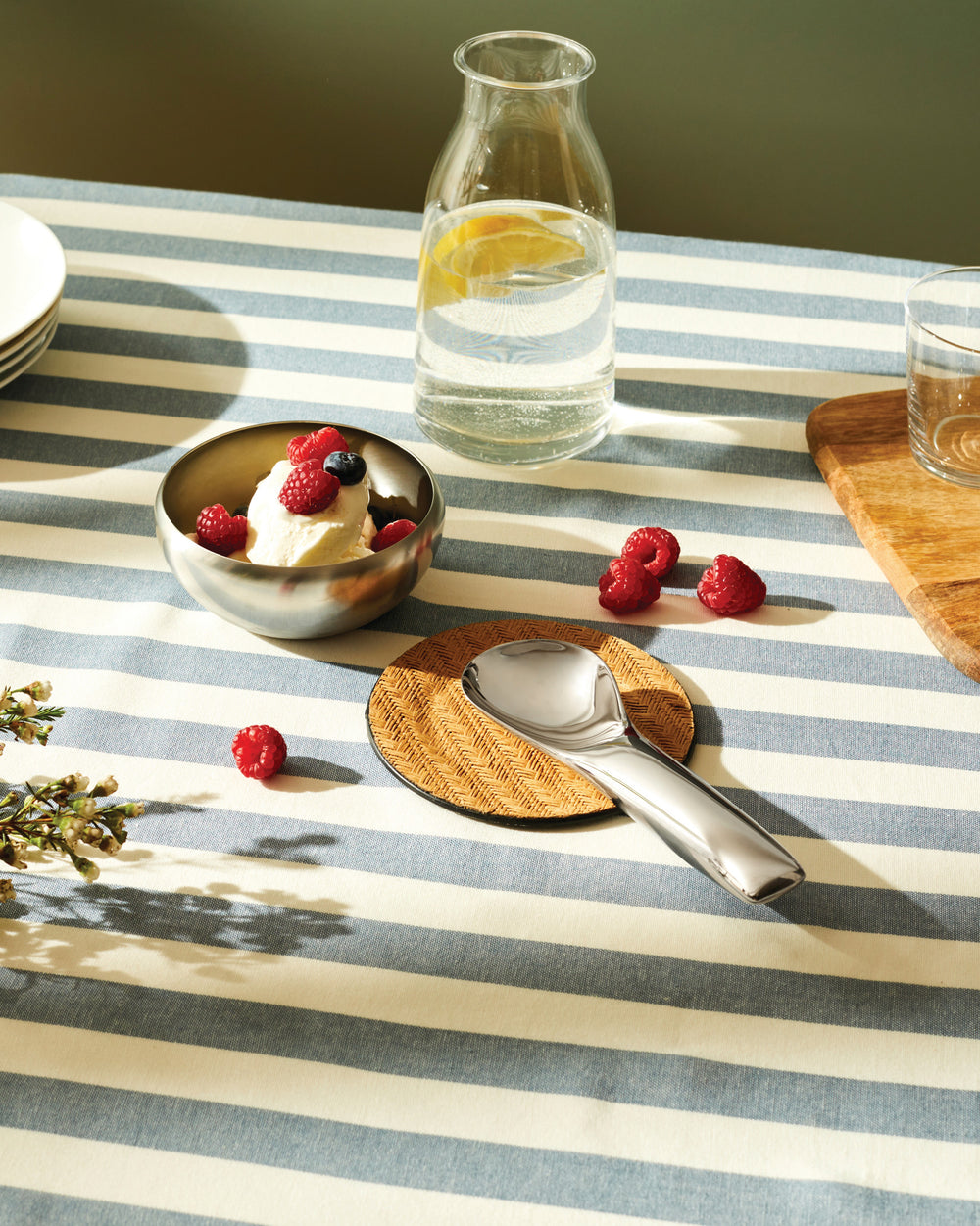 Silver serving spoon by Alessi, resting on a woven coaster next to ice cream and berries.