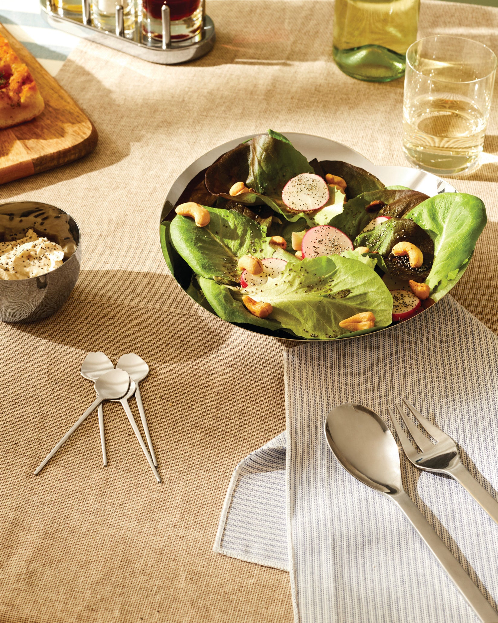 Stainless steel cutlery collection by Alessi, including a serving spoon, fork, and small decorative spoons, on a striped napkin.
