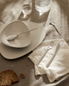 Modern white ceramic plates and sleek cutlery by Alessi on a neutral linen tablecloth.