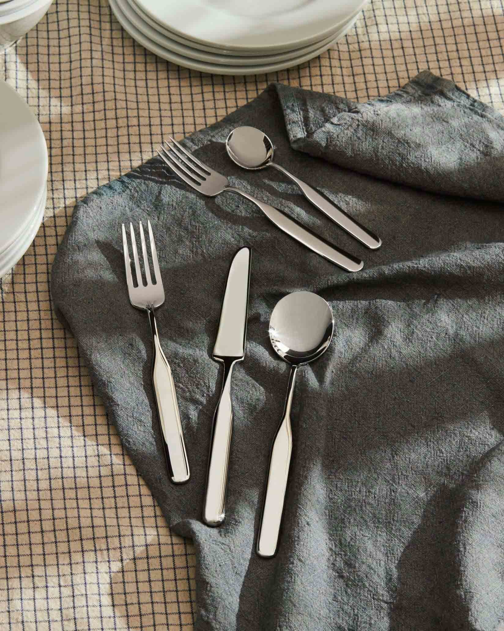 Silver polished Collo-alto cutlery set by Alessi, with a modern, sleek design, arranged on a grey linen napkin.
