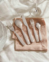 Silver-toned cutlery set by Alessi, featuring ornate relief patterns on the handles, on a pink napkin.