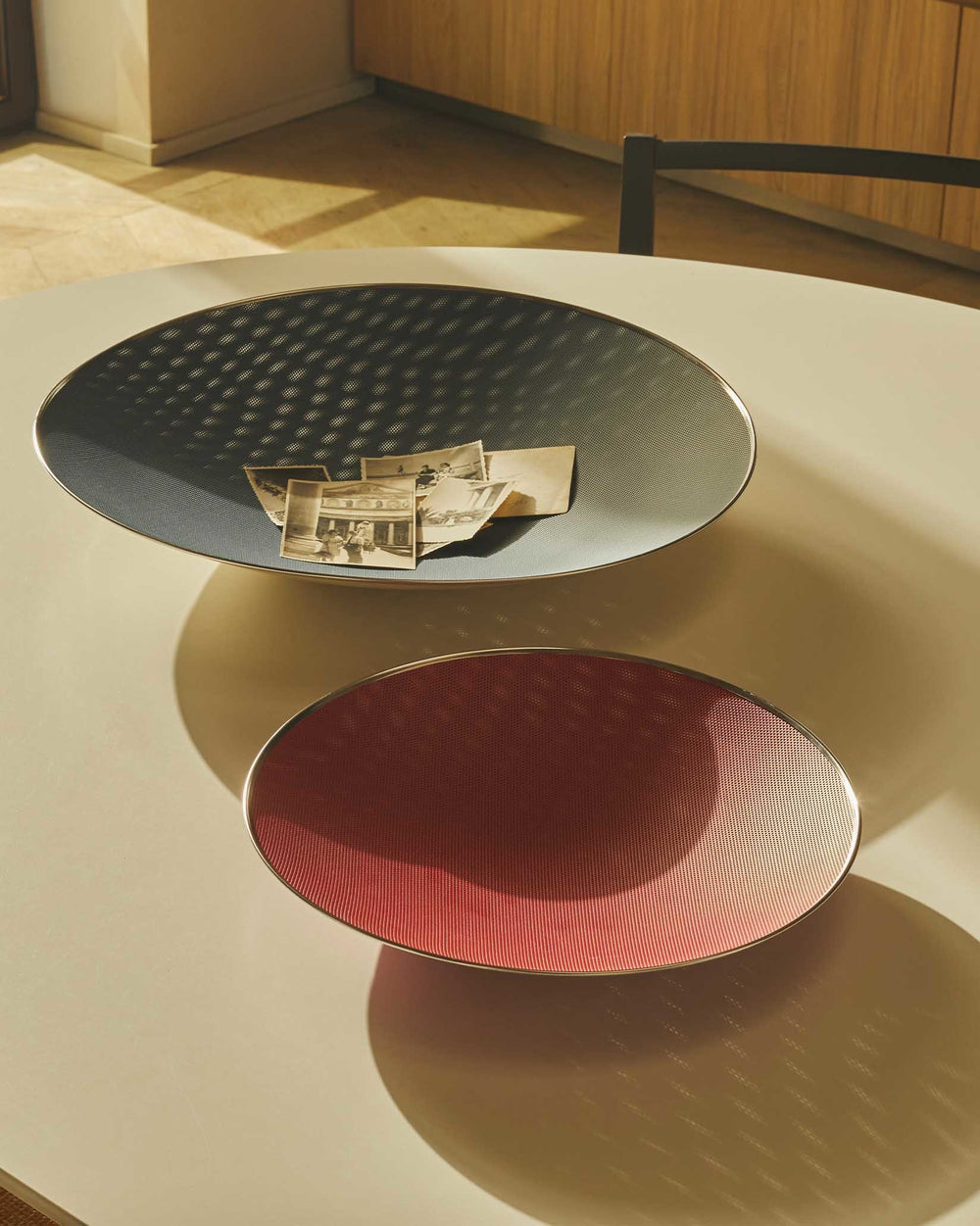 Two dark grey and reddish-pink Cohncave decorative bowls by Alessi, with perforated surfaces and metallic rims, displaying vintage photos.