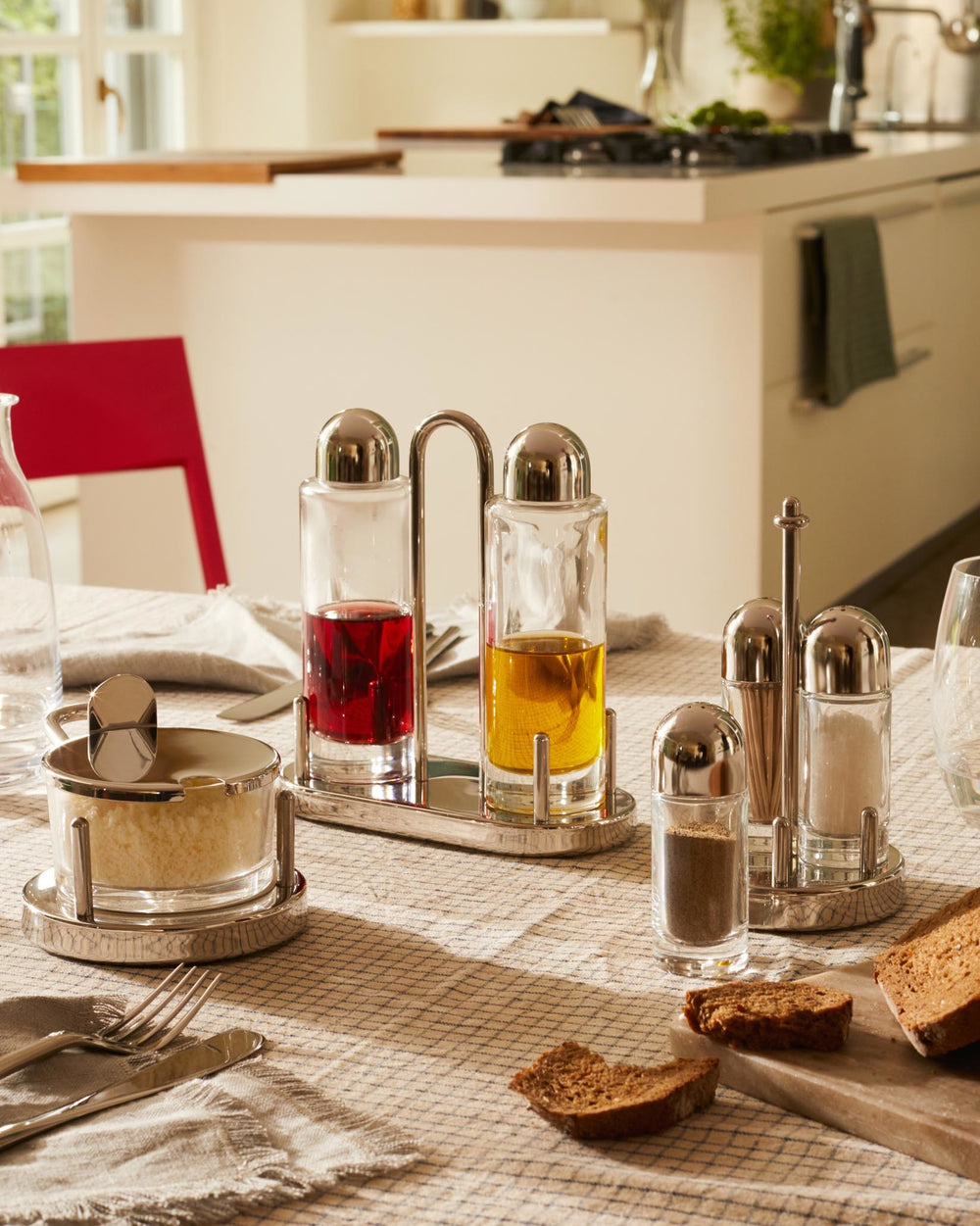 Glass cheese cellar with silver-toned metal base by Alessi, filled with grated cheese, on a checkered dining table.