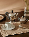 Polished stainless steel Bombé teapot by Alessi, with black handles and knob, displayed with a matching sugar bowl.