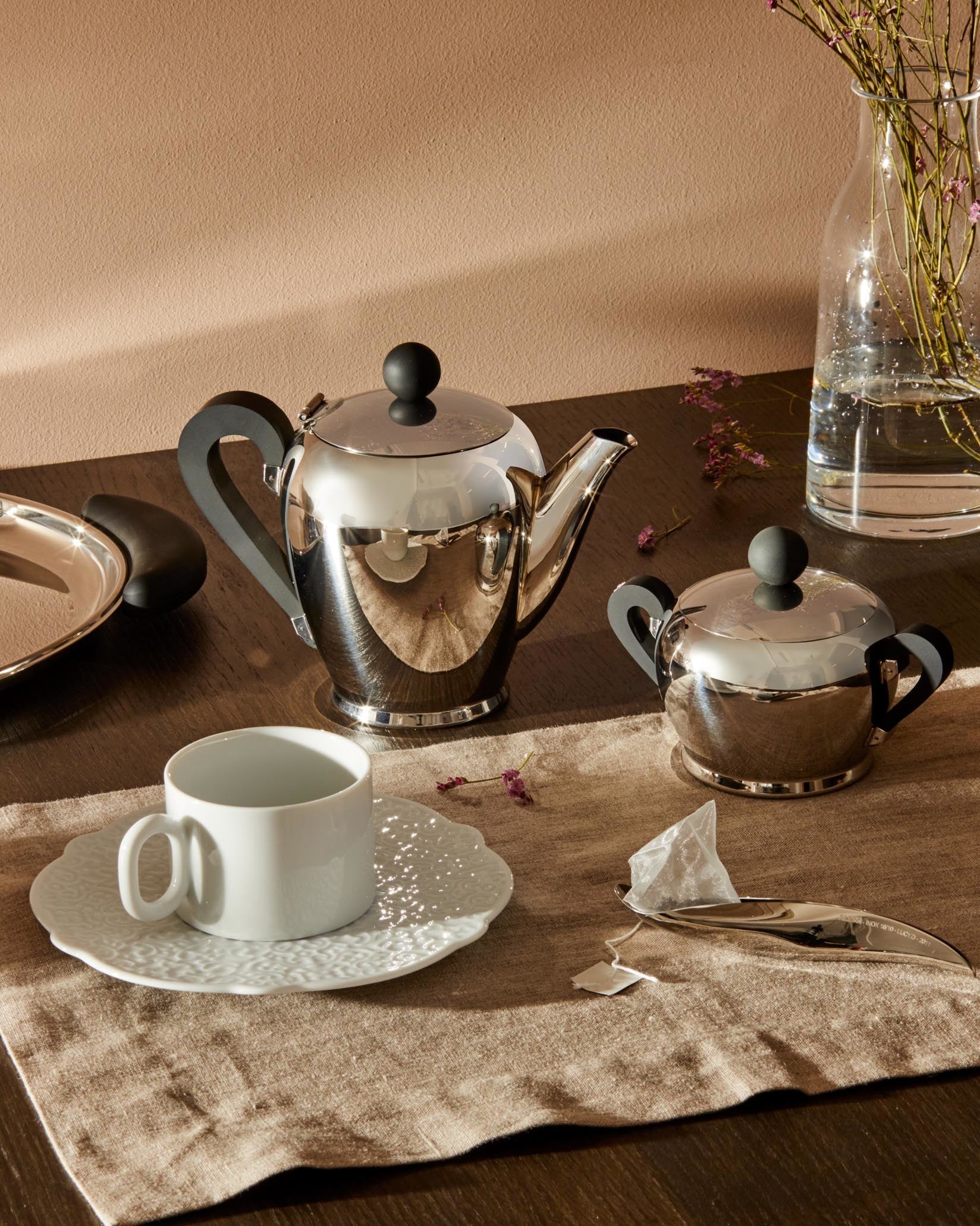 Polished stainless steel Bombé teapot by Alessi, with black handles and knob, displayed with a matching sugar bowl.