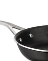 Black non-stick pan by Alessi with a polished metallic handle, rim, and visible rivets, viewed from above.