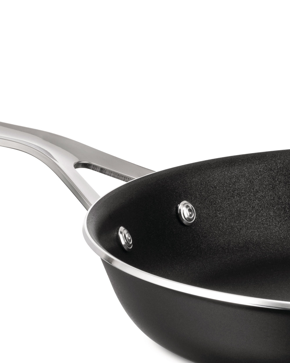 Black non-stick pan by Alessi with a polished metallic handle, rim, and visible rivets, viewed from above.