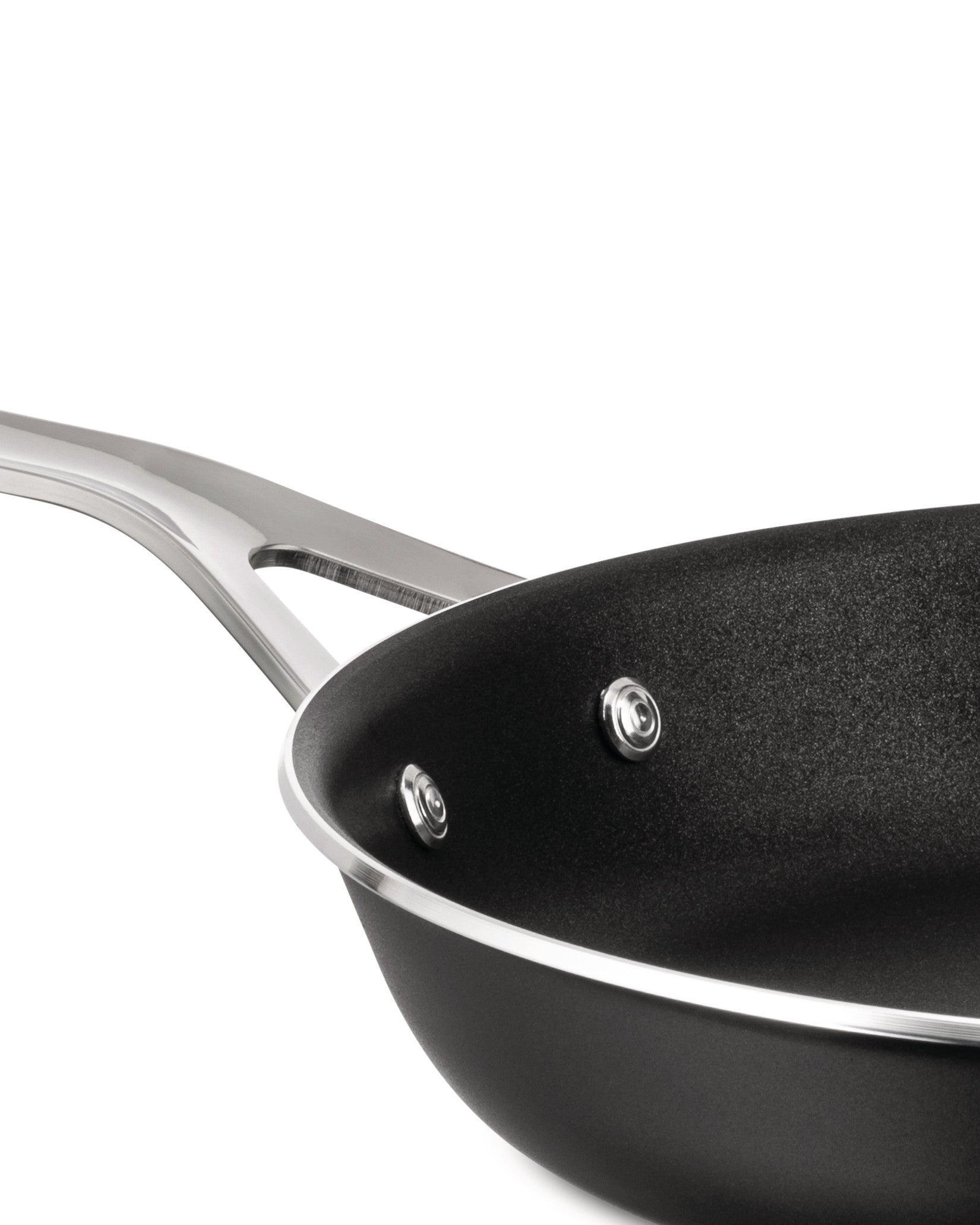 Black non-stick pan by Alessi with a polished metallic handle, rim, and visible rivets, viewed from above.