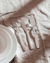 Sparkling silver stainless steel cutlery set by Alessi on a beige fringed linen napkin with white plates.