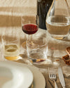 Assorted clear glasses by Alessi, including a red wine glass and tumblers, on a rustic table setting.