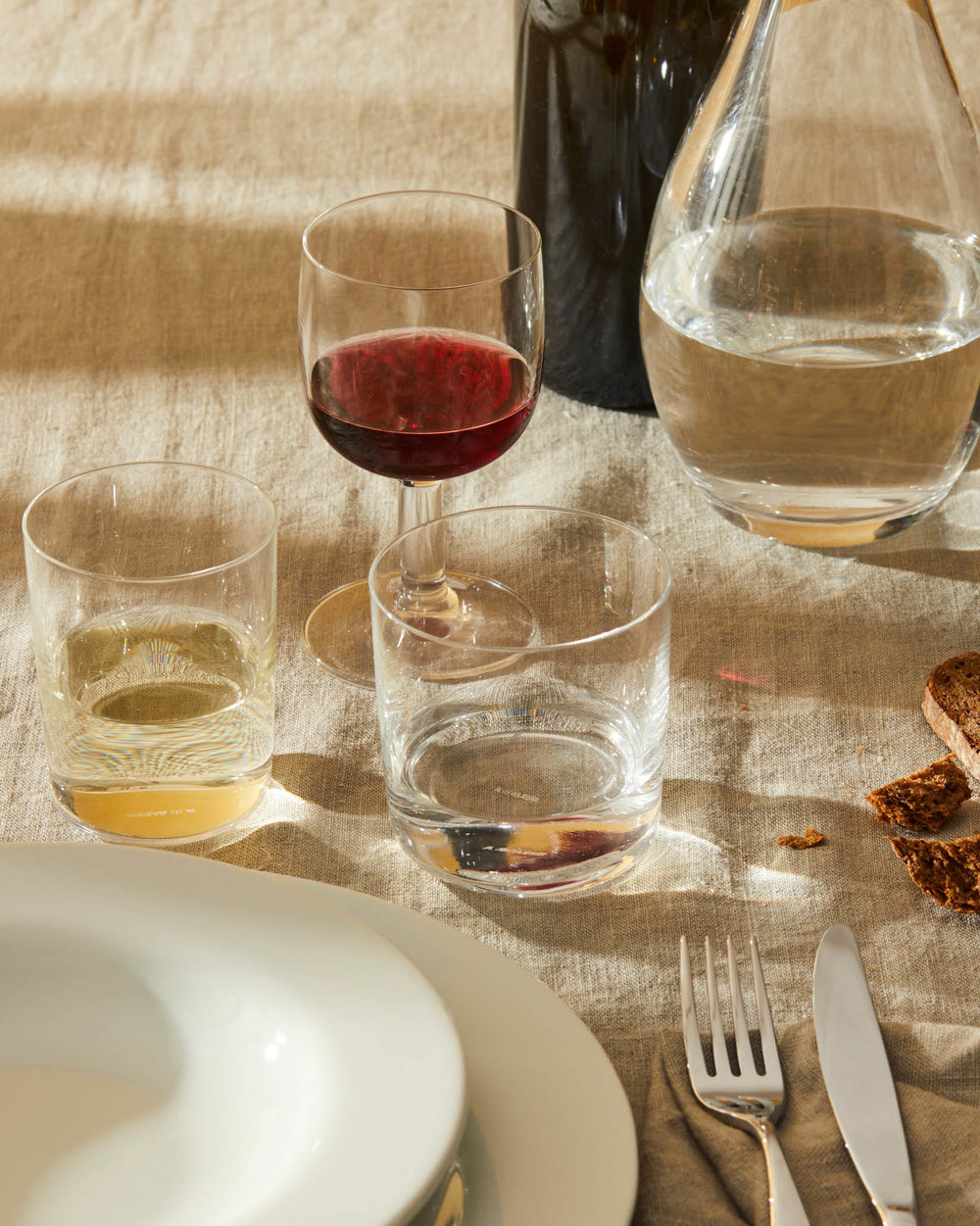 Assorted clear glasses by Alessi, including a red wine glass and tumblers, on a rustic table setting.