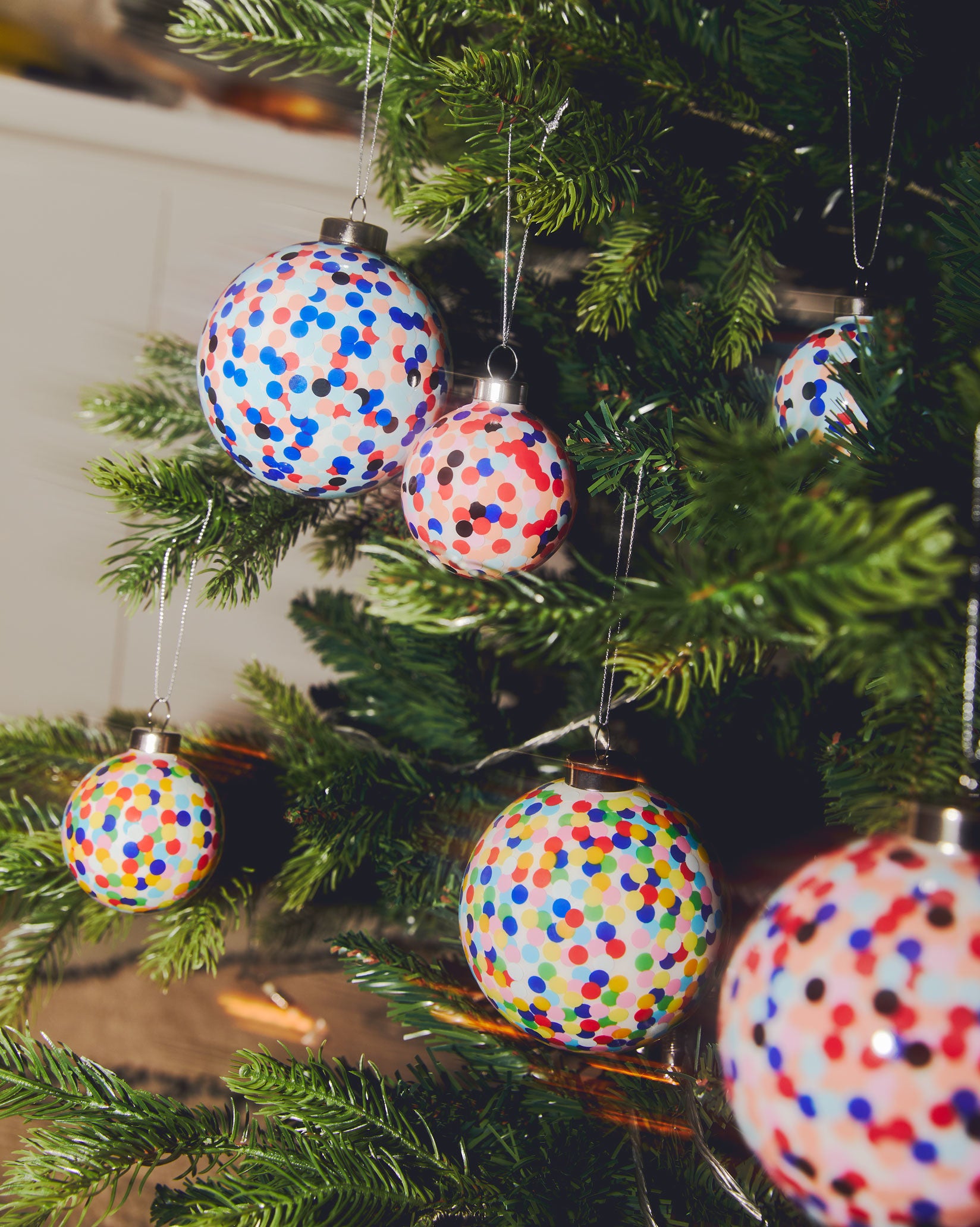 Christmas ornaments with multicolored confetti dots by Alessi, hanging on a green tree.