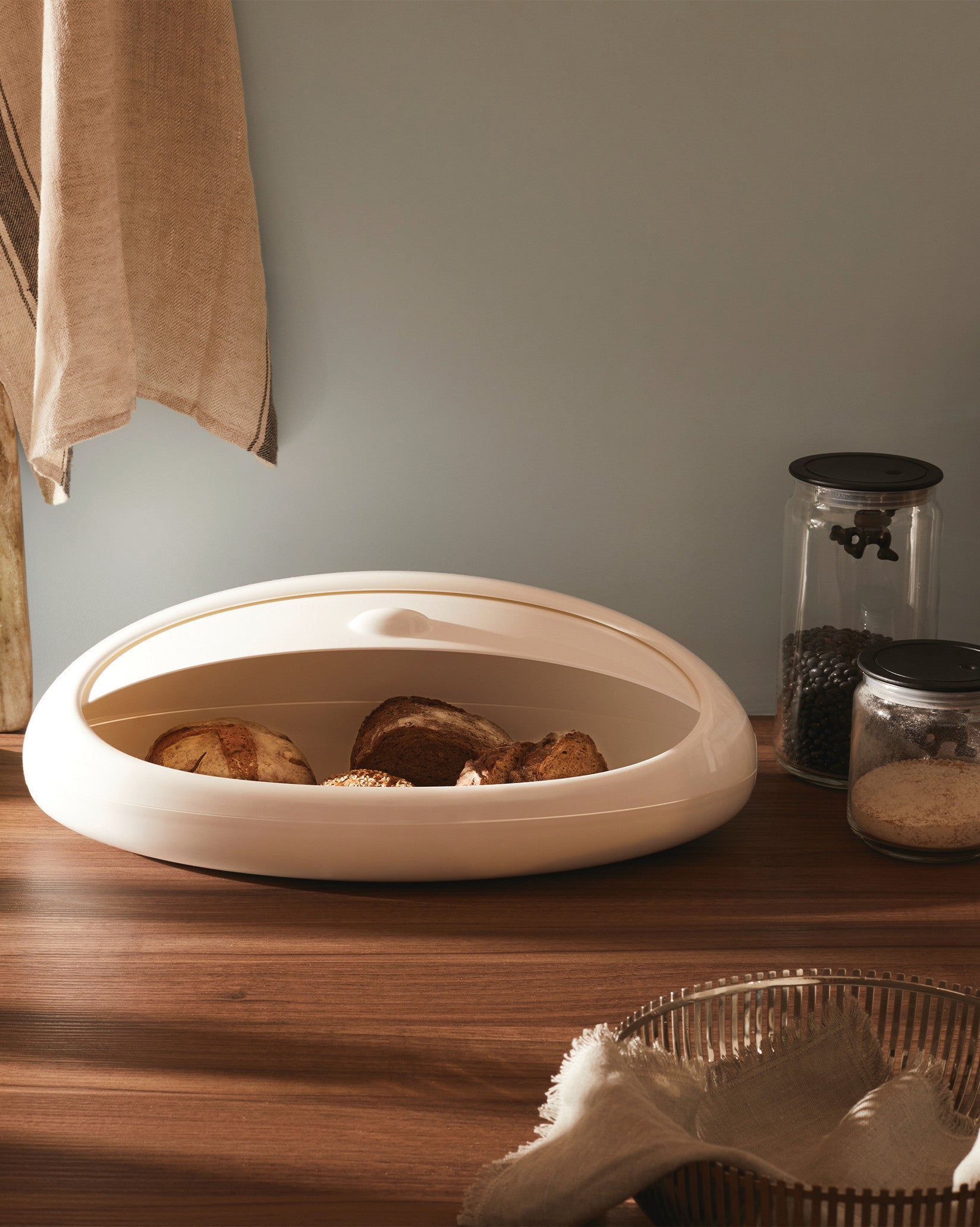 Oval white Gnam bread bin by Alessi, a modern design open with bread inside on a wooden counter.