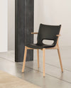 Black molded chair by Alessi with a natural wood frame, short armrests, and cutout back, on a concrete floor with a beige rug.