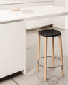 Black seat bar stool with natural wood legs by Alessi, featuring a silver footrest in a modern kitchen.