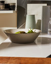 Beige ceramic Tonale bowl by Alessi holding green peppers on a modern white counter.