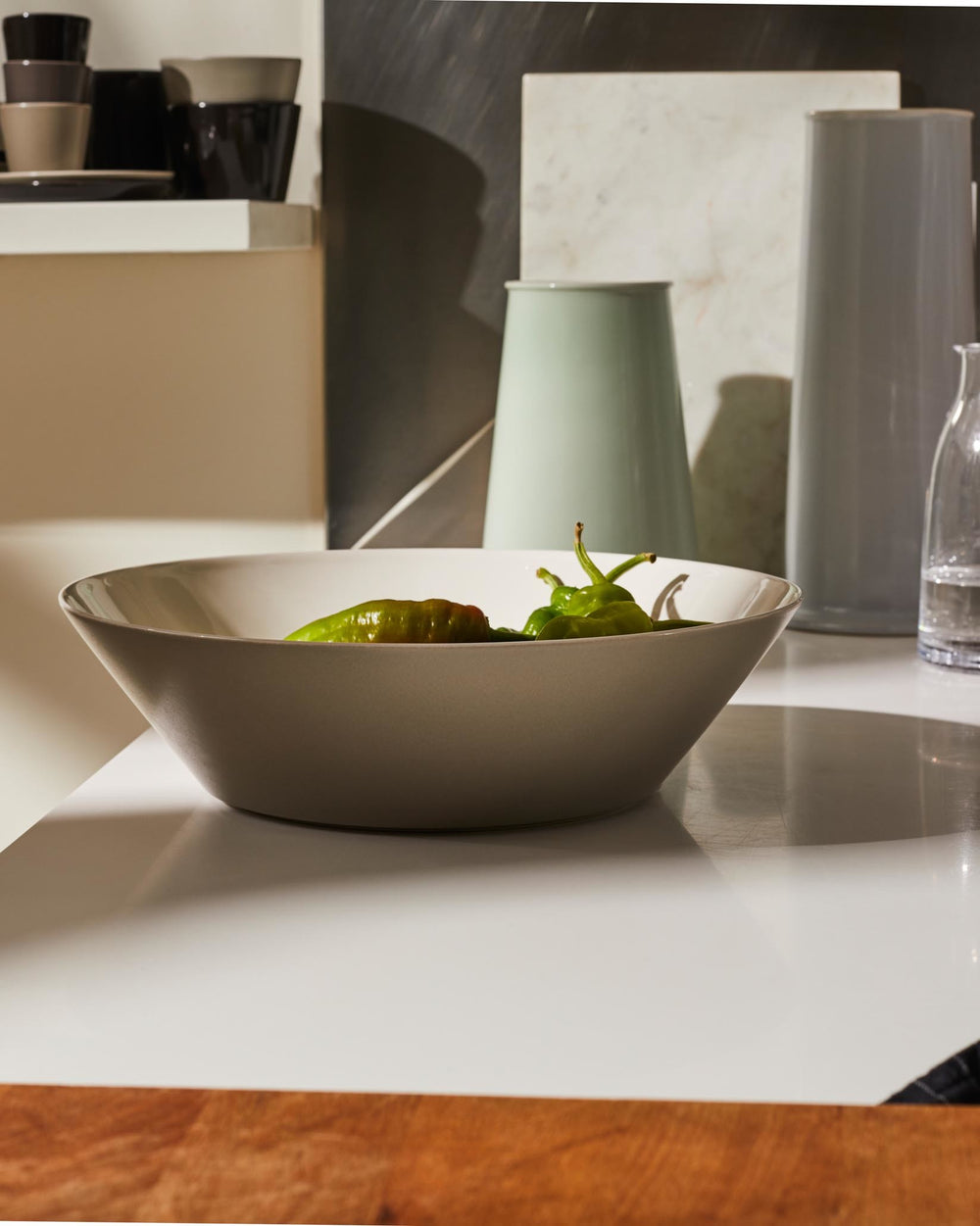 Beige ceramic Tonale bowl by Alessi holding green peppers on a modern white counter.