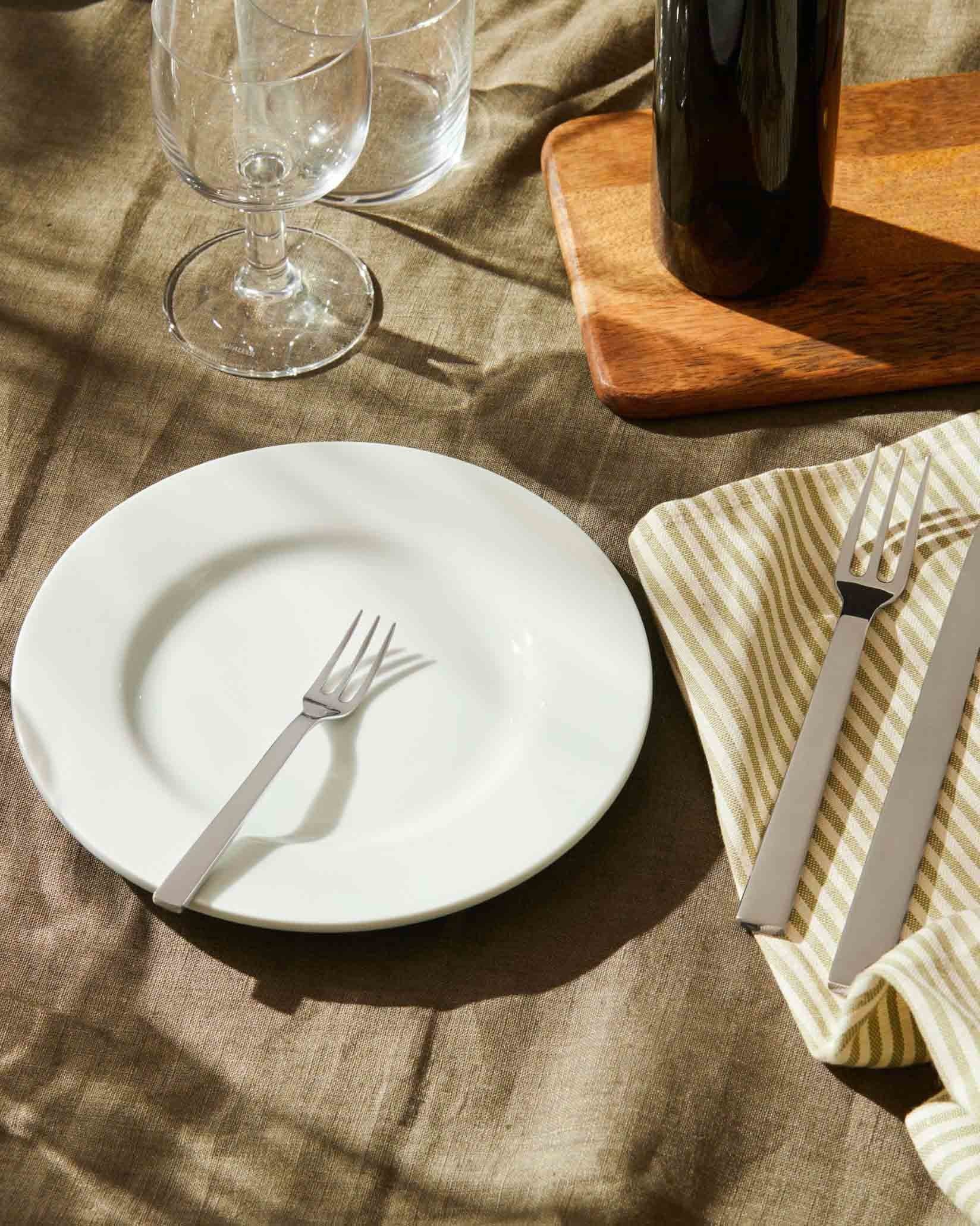 Santiago stainless steel cutlery by Alessi, with a fork on a white plate and knife on a striped napkin.