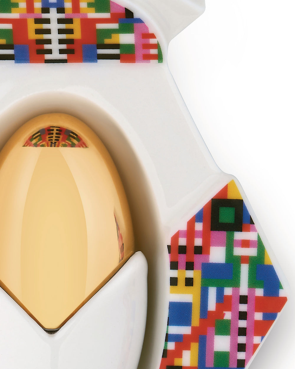 Golden egg-shaped Holyhedrics Jesus by Alessi in a white holder with colorful geometric pixel patterns.
