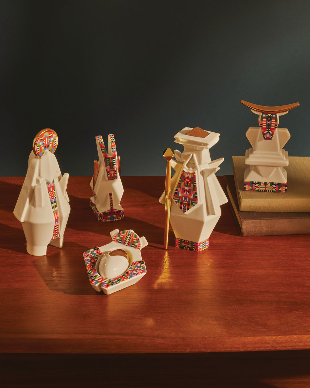 White ceramic geometric cow figure by Alessi, with colorful pixelated patterns and gold horns, on a wooden surface.