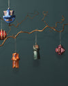 A dark green bell-shaped Christmas tree ornament by Alessi, with colorful pixel patterns, hanging from a branch.
