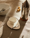 White ceramic Colombina collection tableware by Alessi, with an asymmetrical bowl and plate on a textured linen tablecloth.