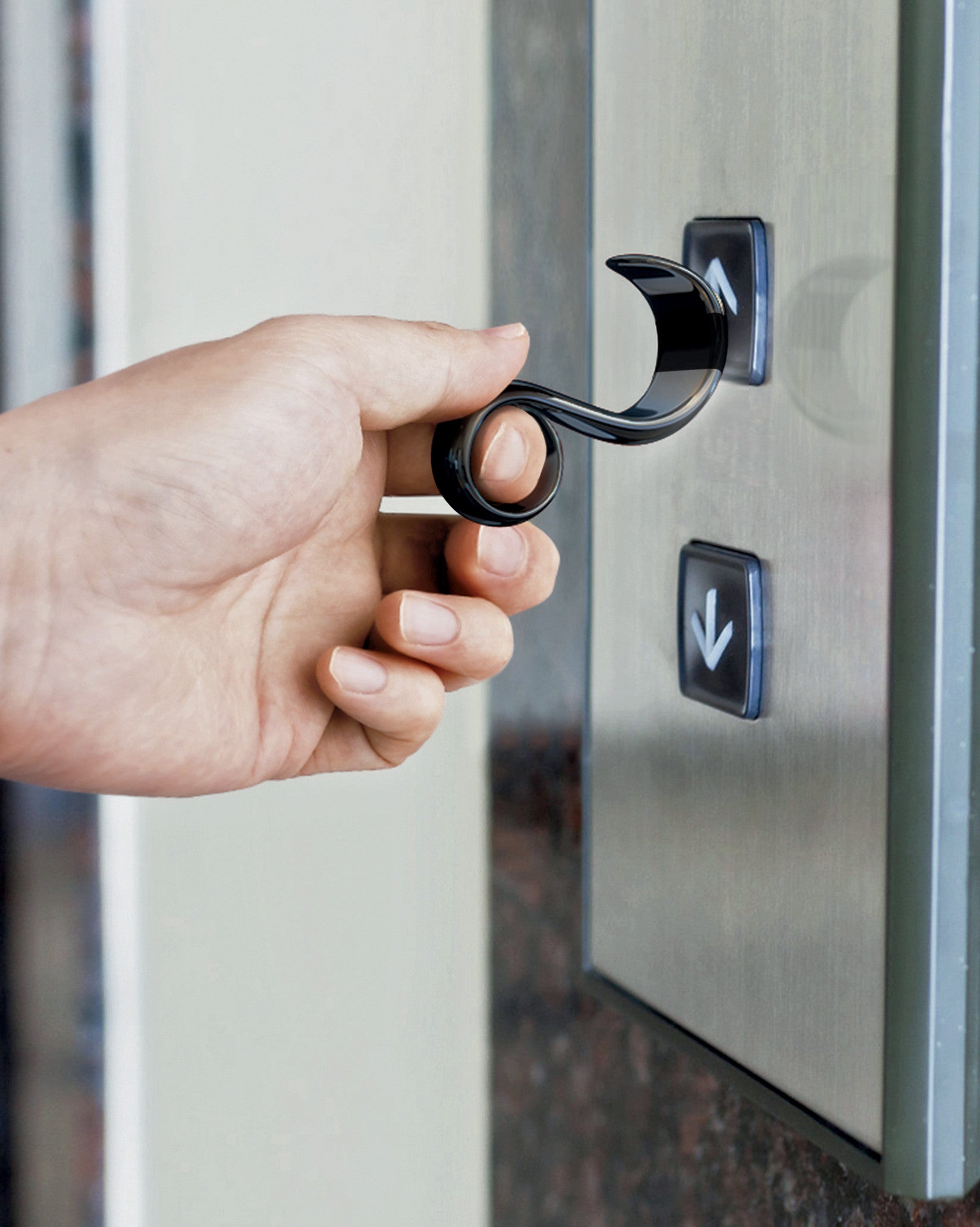 Black curved touchless tool by Alessi held by a hand to press an elevator up button.